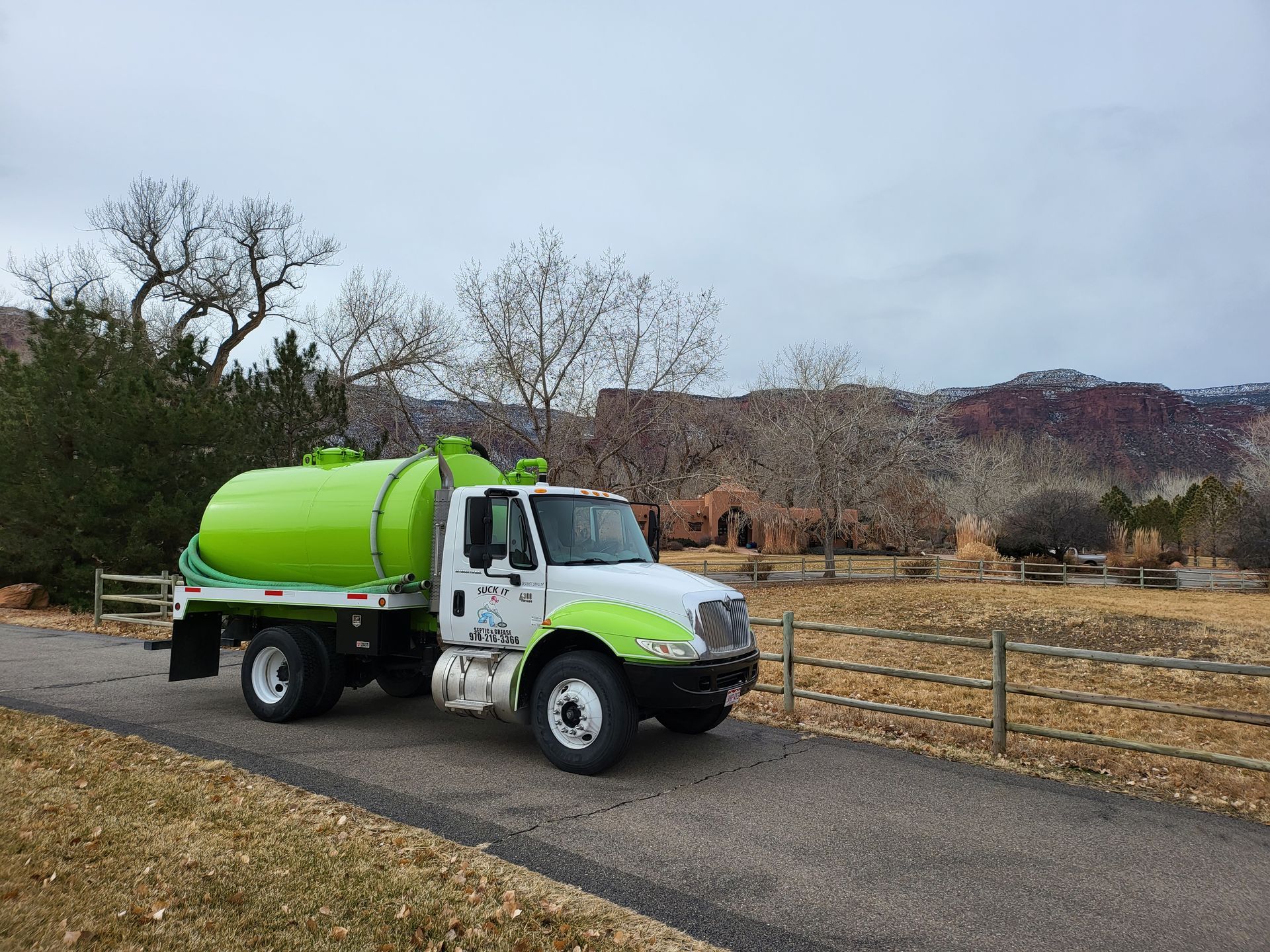 Bright green tanker truck parked on a rural road beside a wooden fence and dry fields