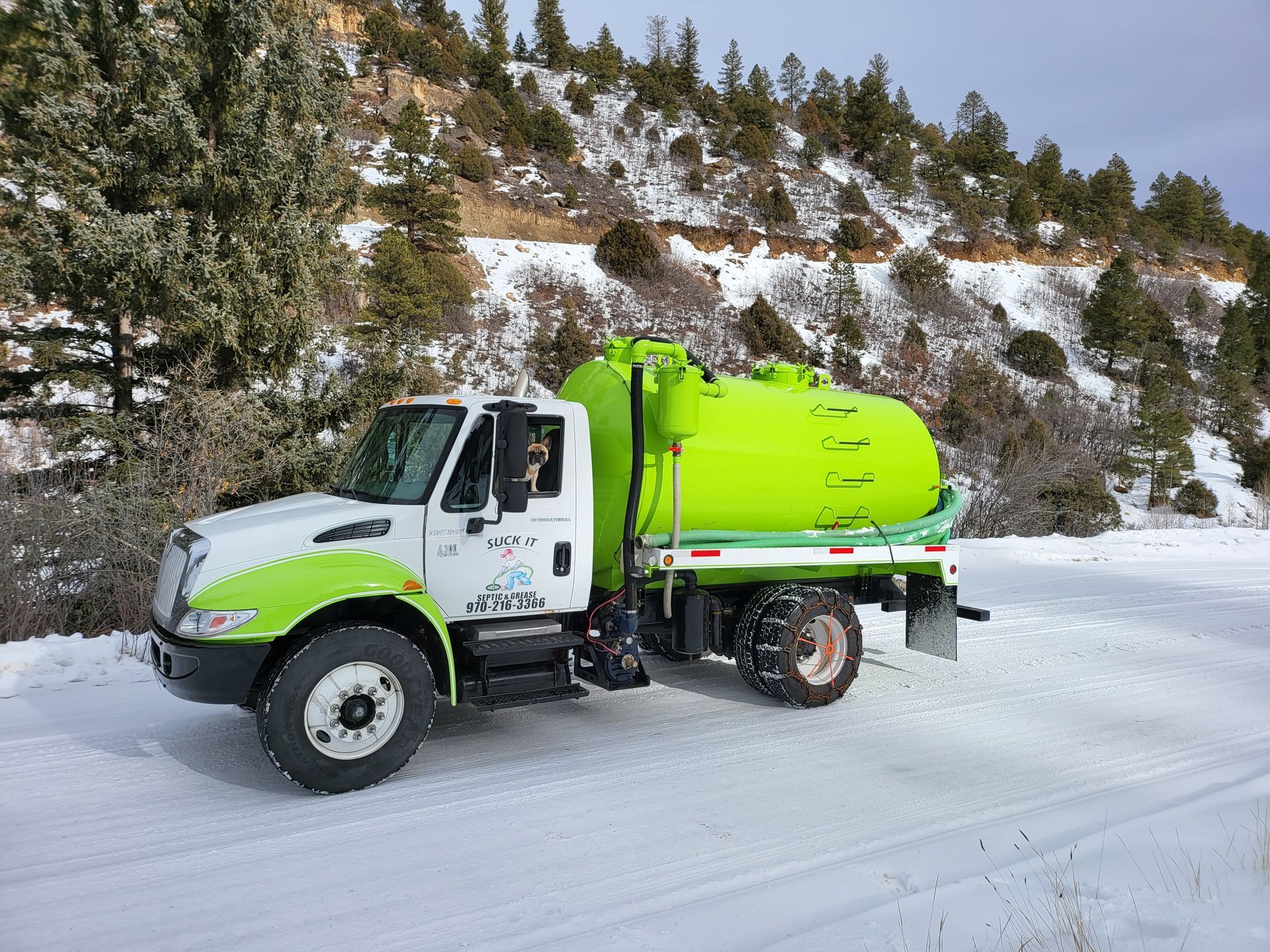 Lime-green tanker truck on a snowy road beside a forested hillside