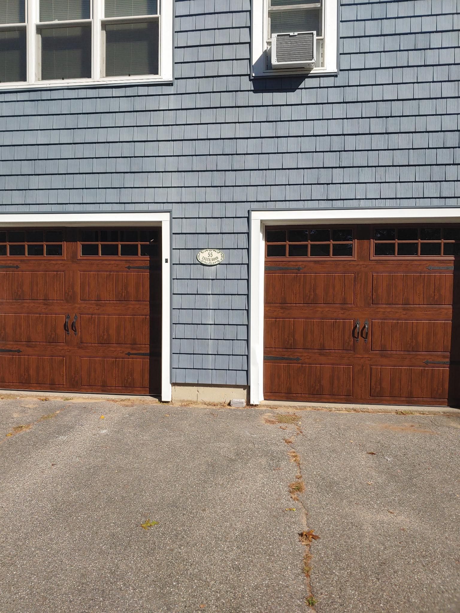 Two brown garage doors with white trim, blue siding, and an air conditioner.