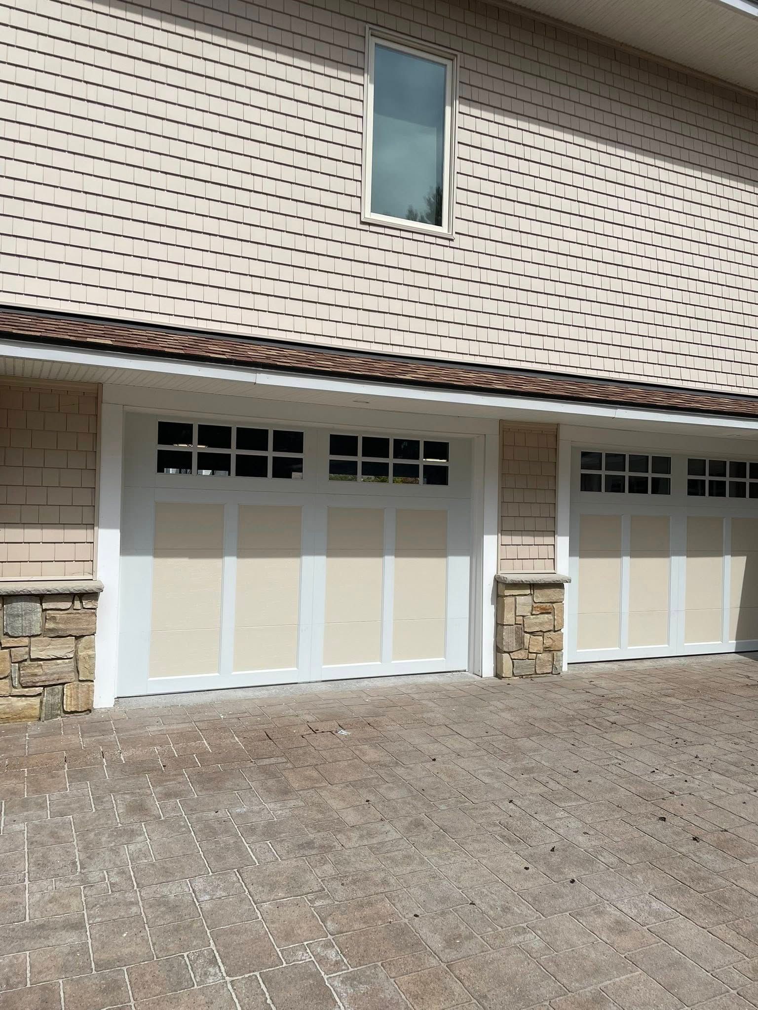 Two beige garage doors with white trim and a stone facade. Light tan siding on the building.