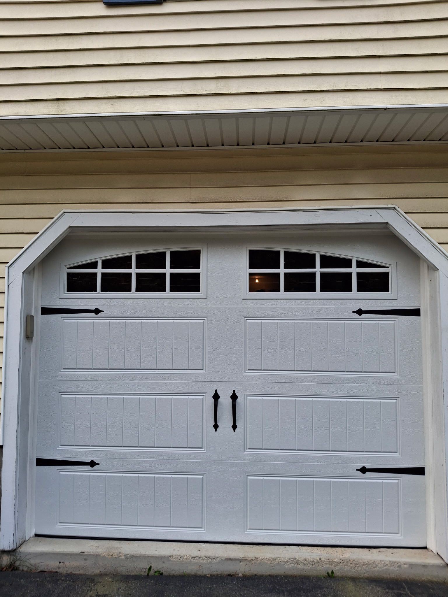 White garage door with black hardware; windows at top, set against yellow siding.