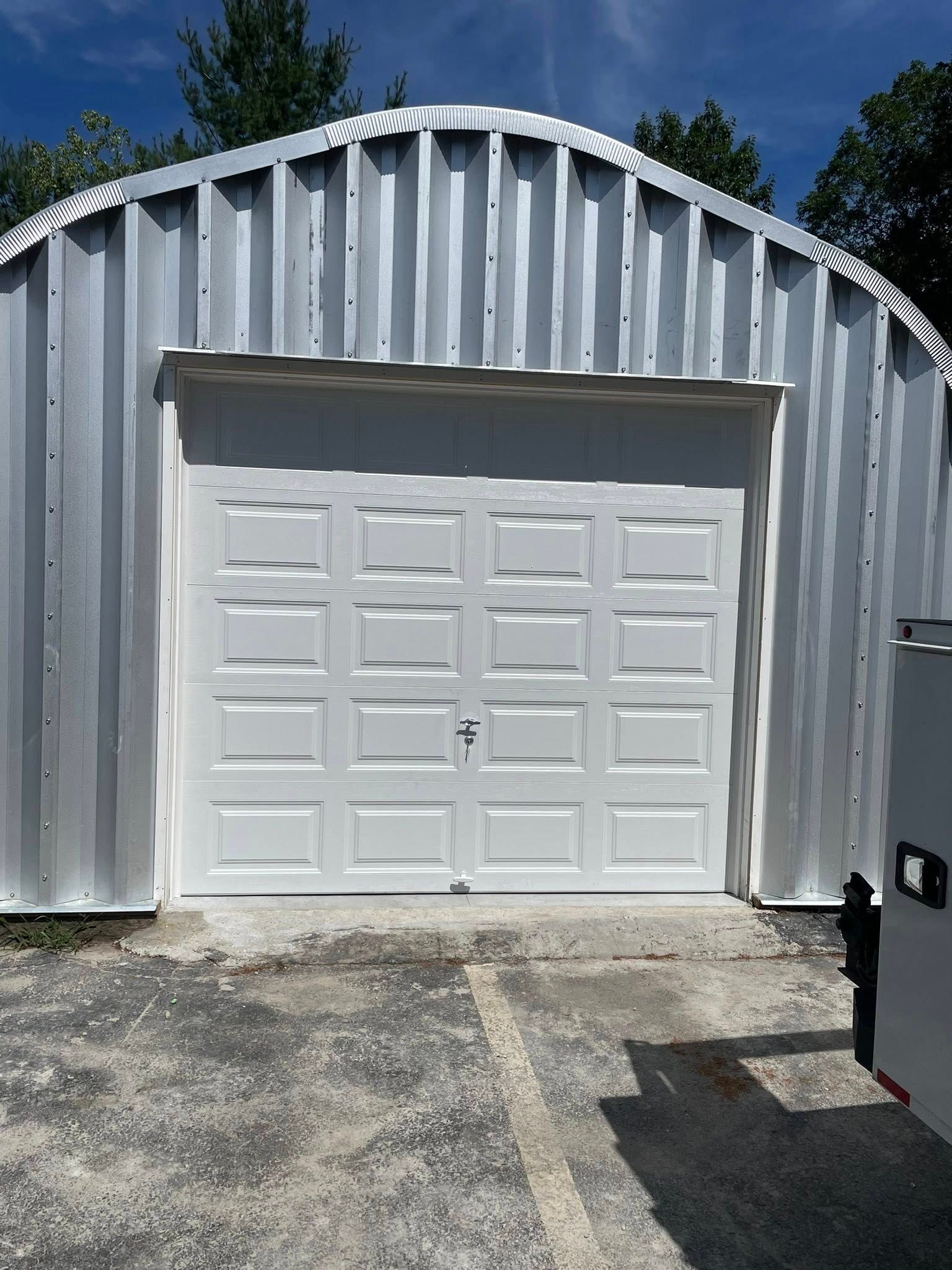 White garage door in a metal building. Concrete driveway. Blue sky.