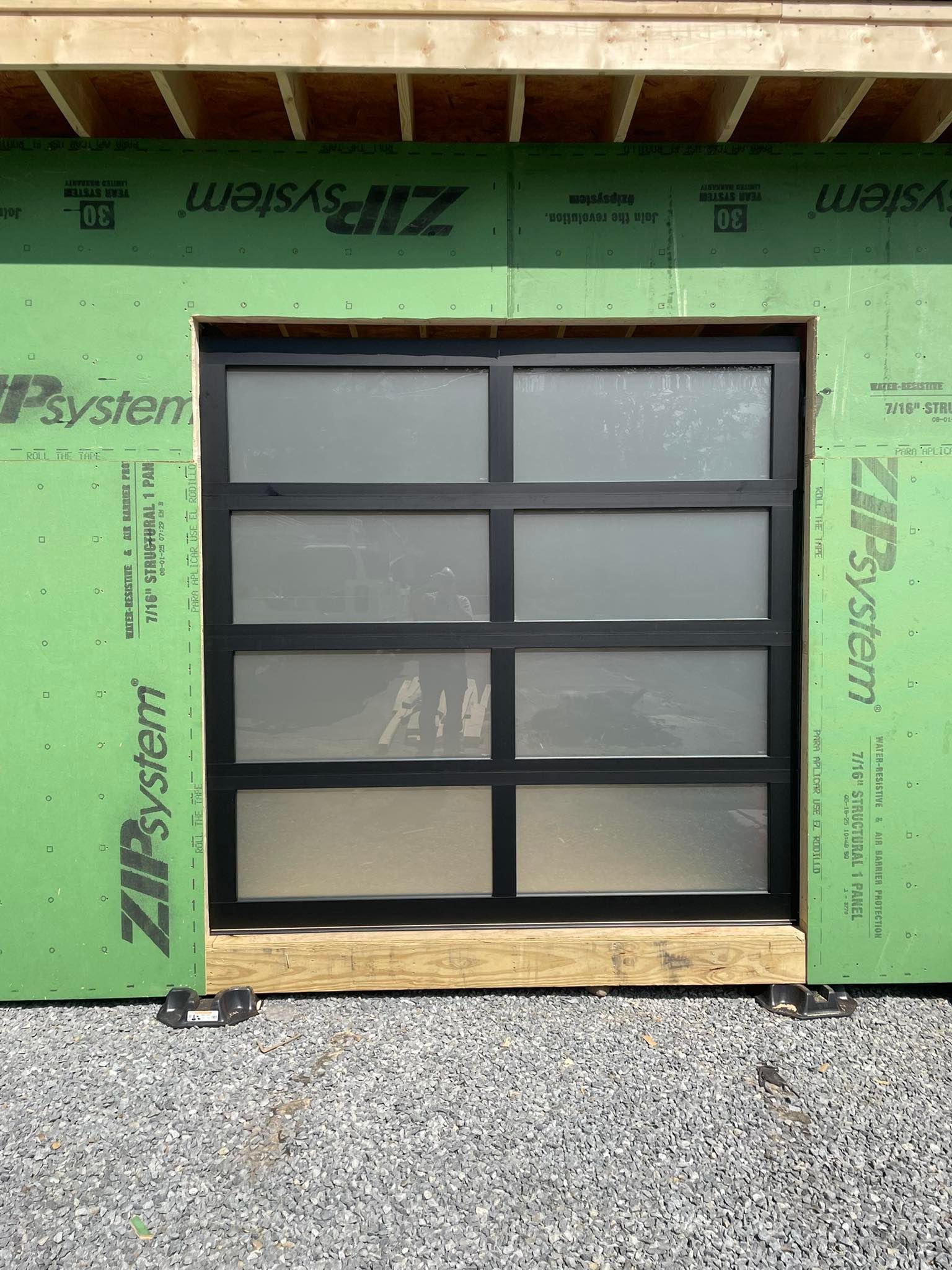 Modern black-framed garage door with eight frosted glass panes, set in a building under construction.