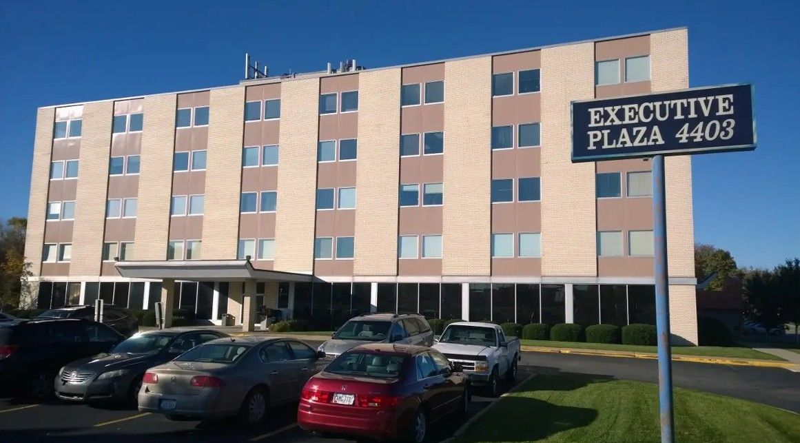 Executive Plaza building with a sign, cars parked in front, and a blue sky.