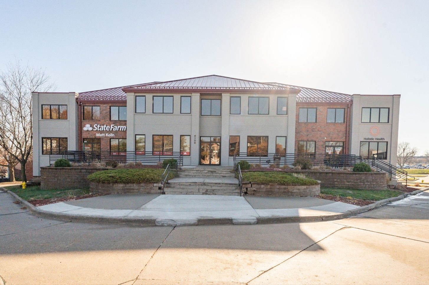 Office building with a red tile roof, brick accents, and a small front garden under a sunny sky.
