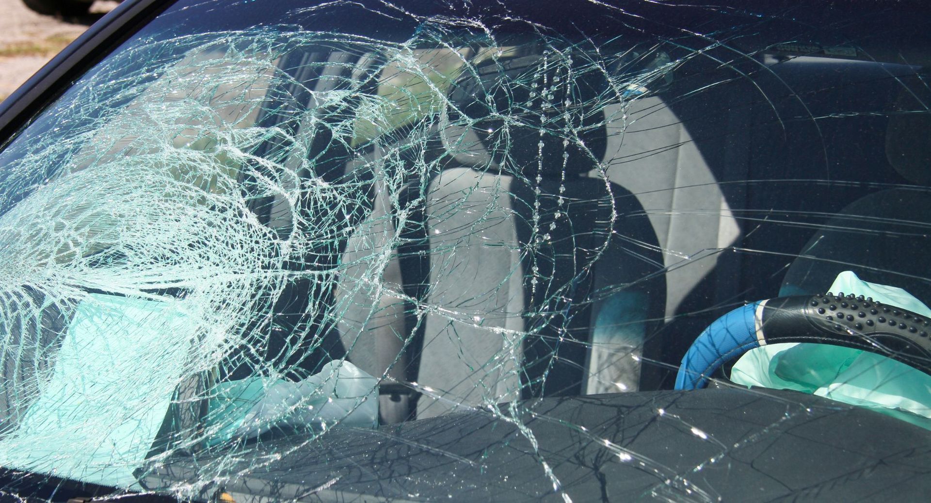 Severely cracked windshield on a car, with shattered glass spiderwebbing across the front.