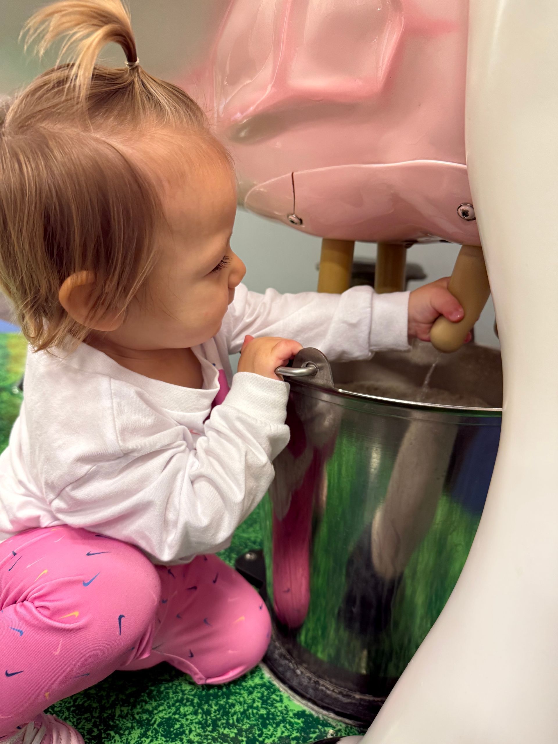 A little girl in pink pants is playing with a bucket.