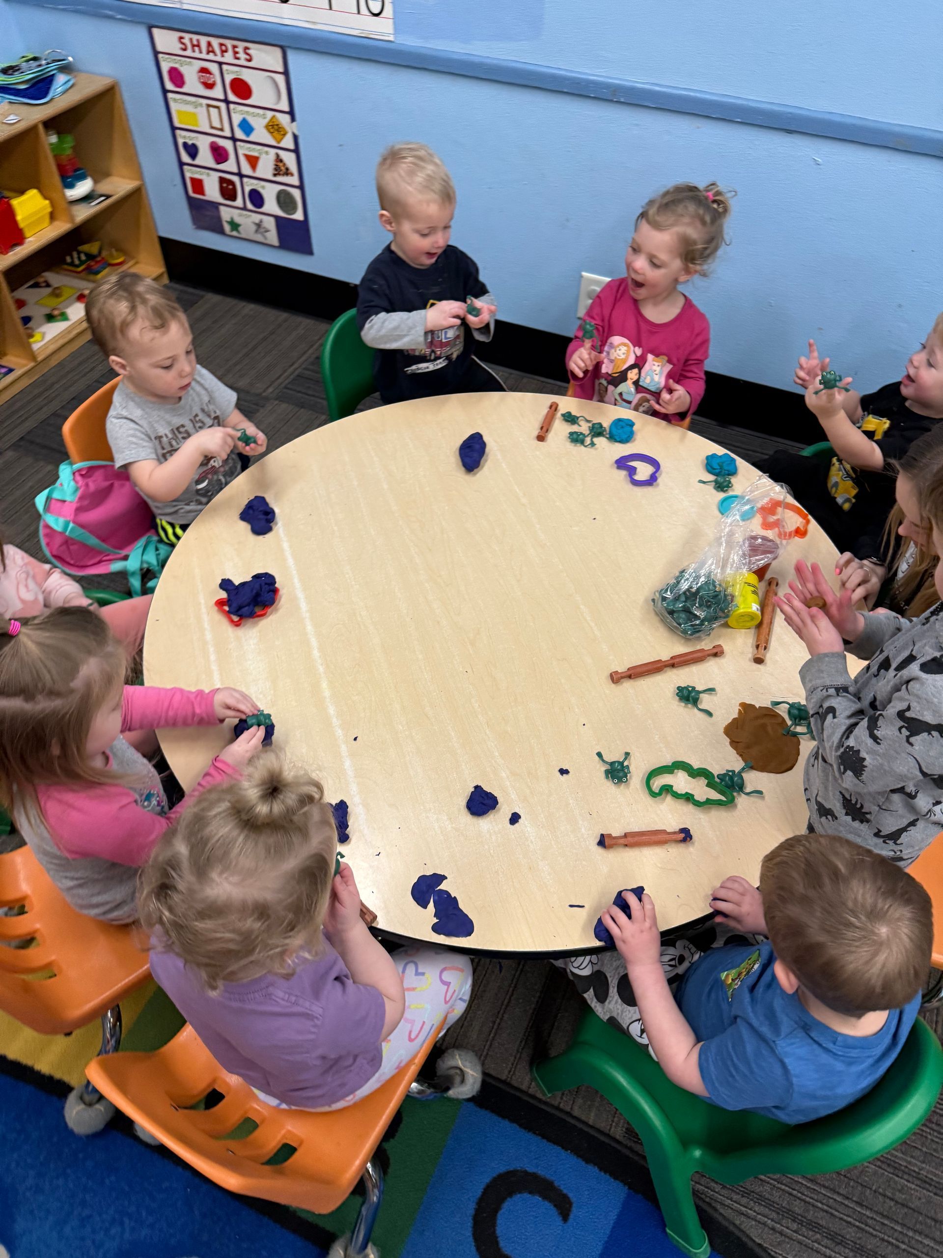 A group of children is sitting around a table playing with play dough