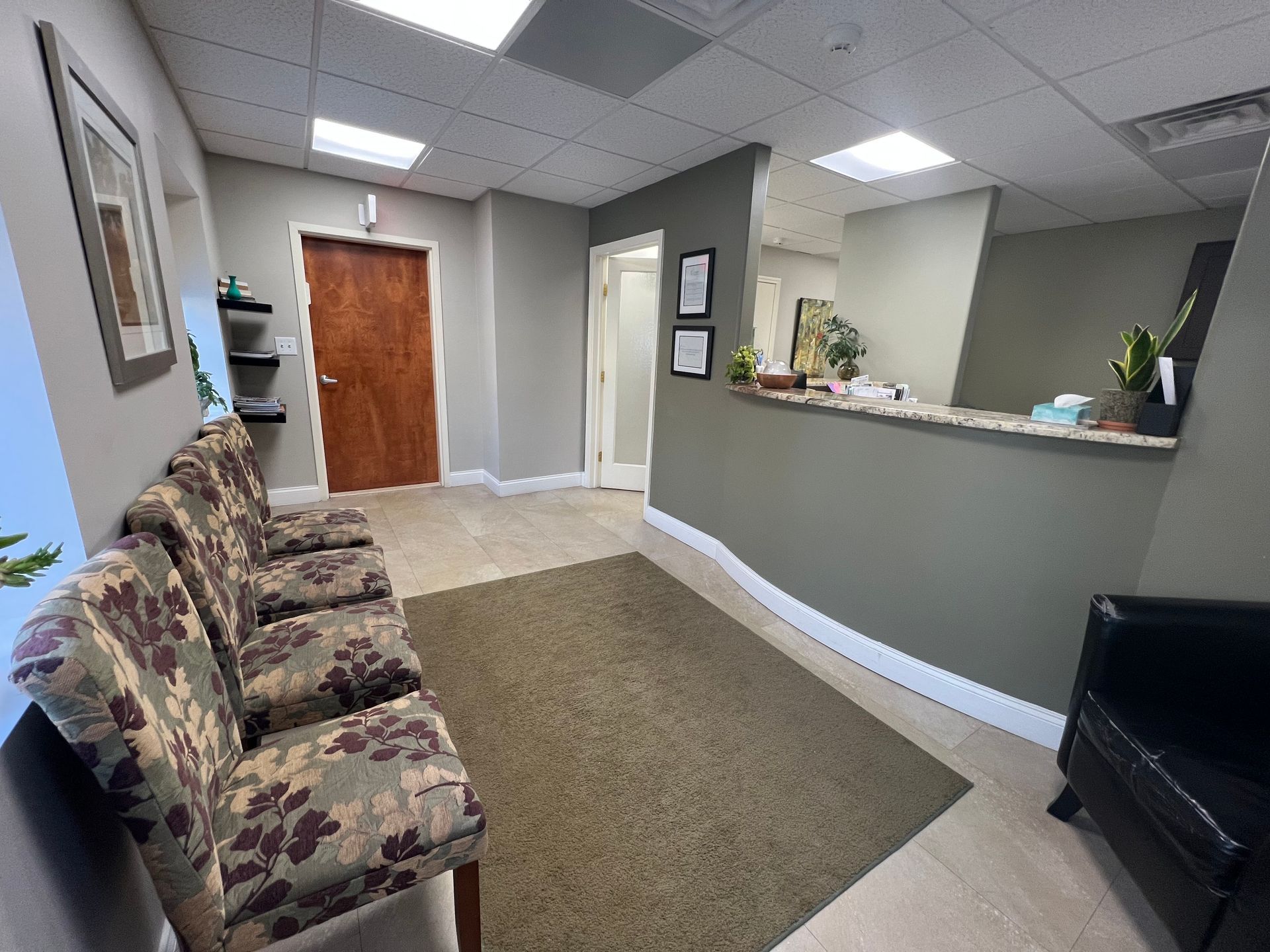 A waiting room with four patterned chairs, windows with shades, and a framed picture.