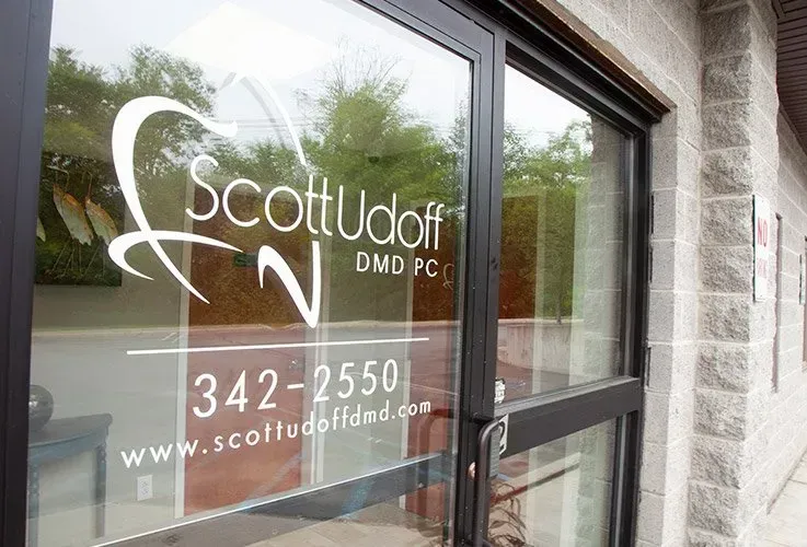 Exterior of Scott Udoff, DMD PC dental office with logo on glass door, phone number, and website.