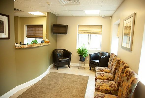 Waiting room with brown and olive green walls, two black chairs, patterned sofa, and window with blinds.