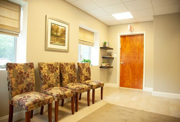 A waiting room with four patterned chairs, windows with shades, and a framed picture.