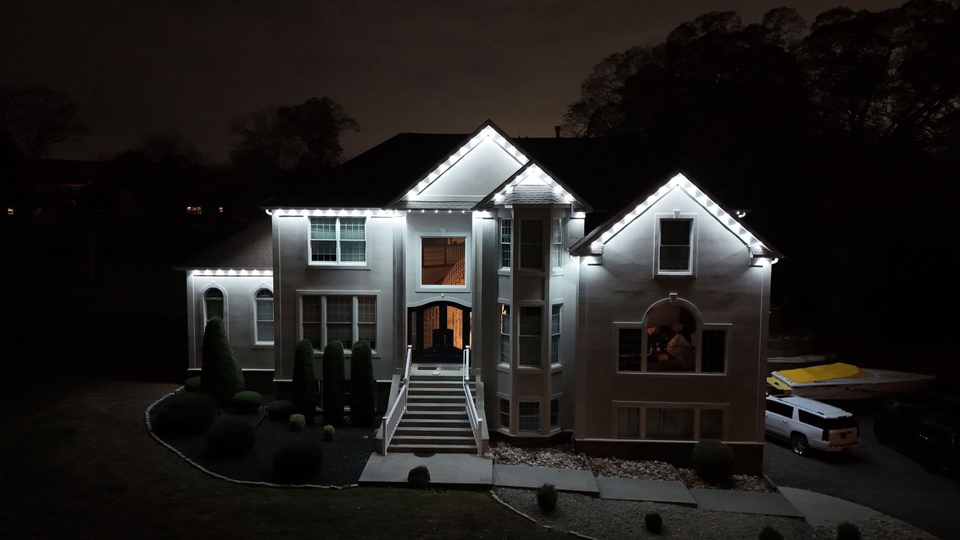 Large two-story house at night, brightly lit from the front, with steps and a parked car on the right.