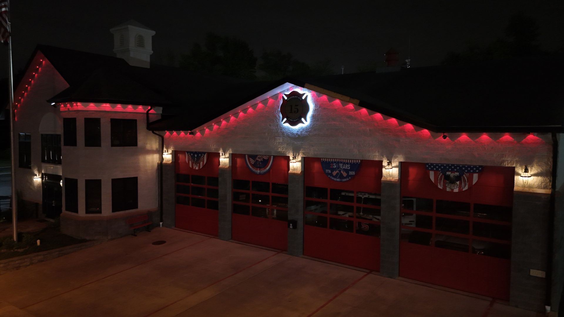 Red-lit fire station at night with wreath and holiday garlands across the garage doors