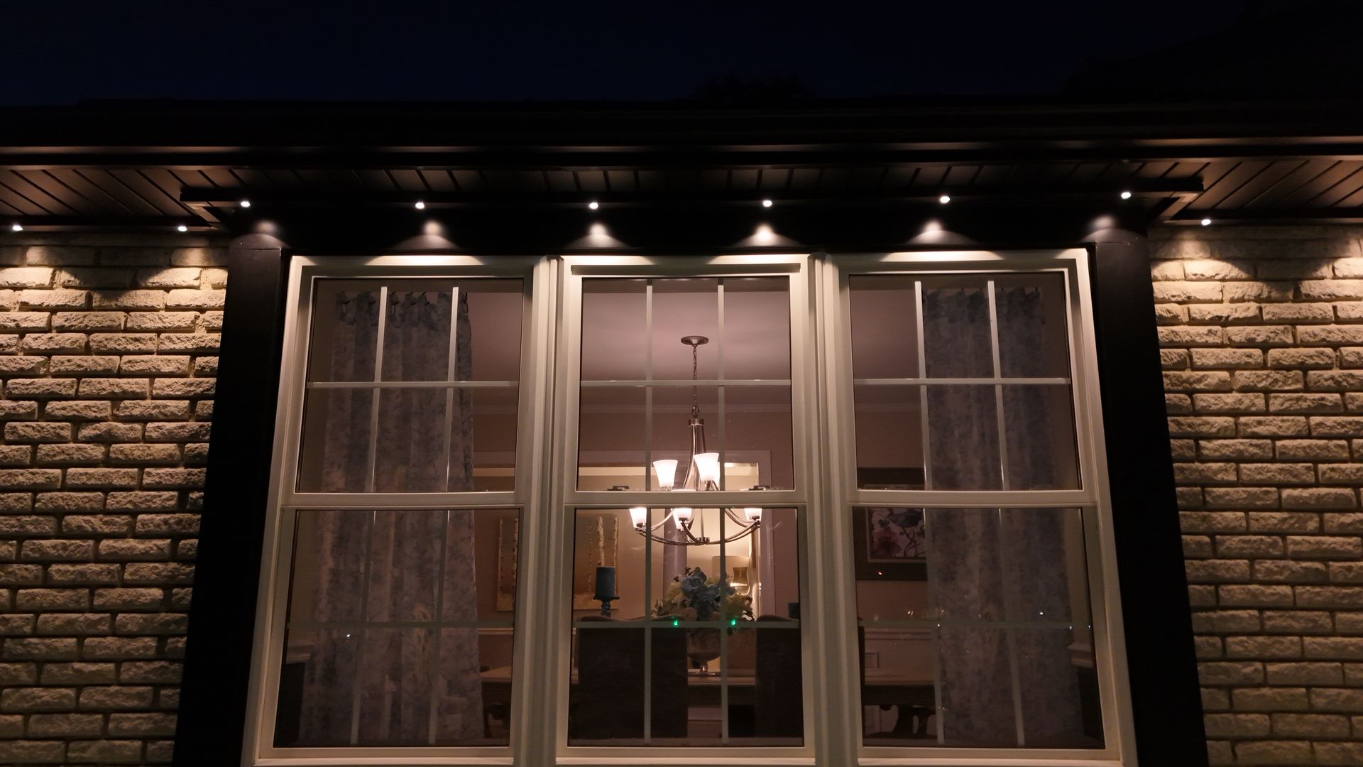 Illuminated brick house facade with a large window showing a warmly lit interior
