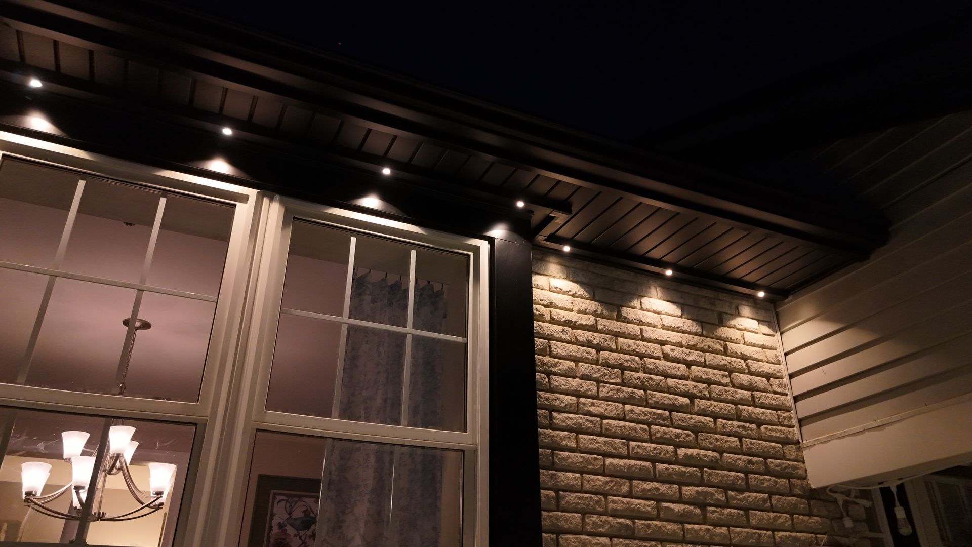Front porch at night with warm lights, white windows, and a brick wall.