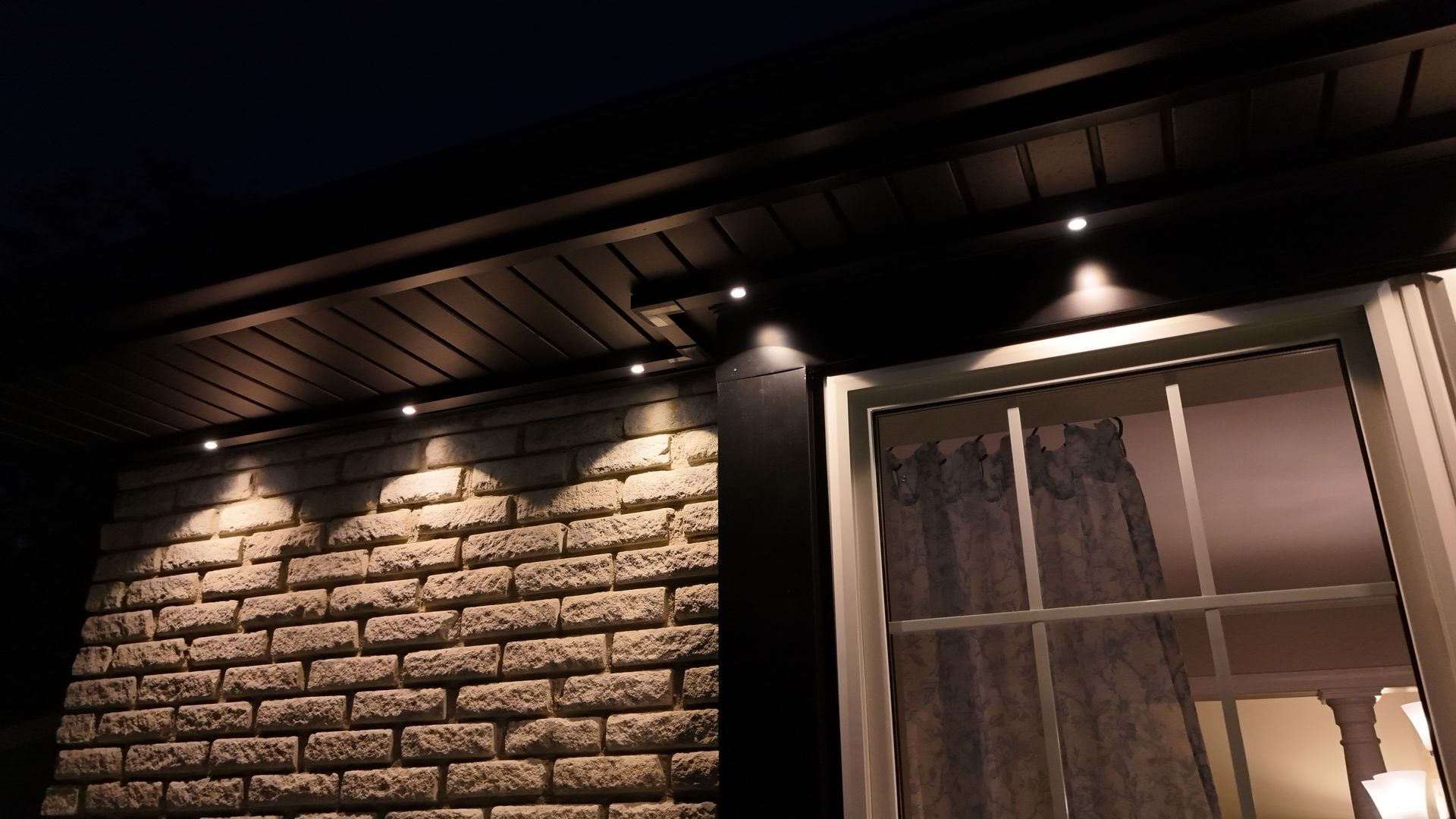 Brick house exterior at night with warm porch lights and a window lit from inside