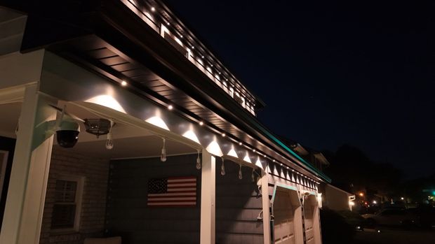 Nighttime exterior of a building with lit roofline lights and an American flag on the wall.