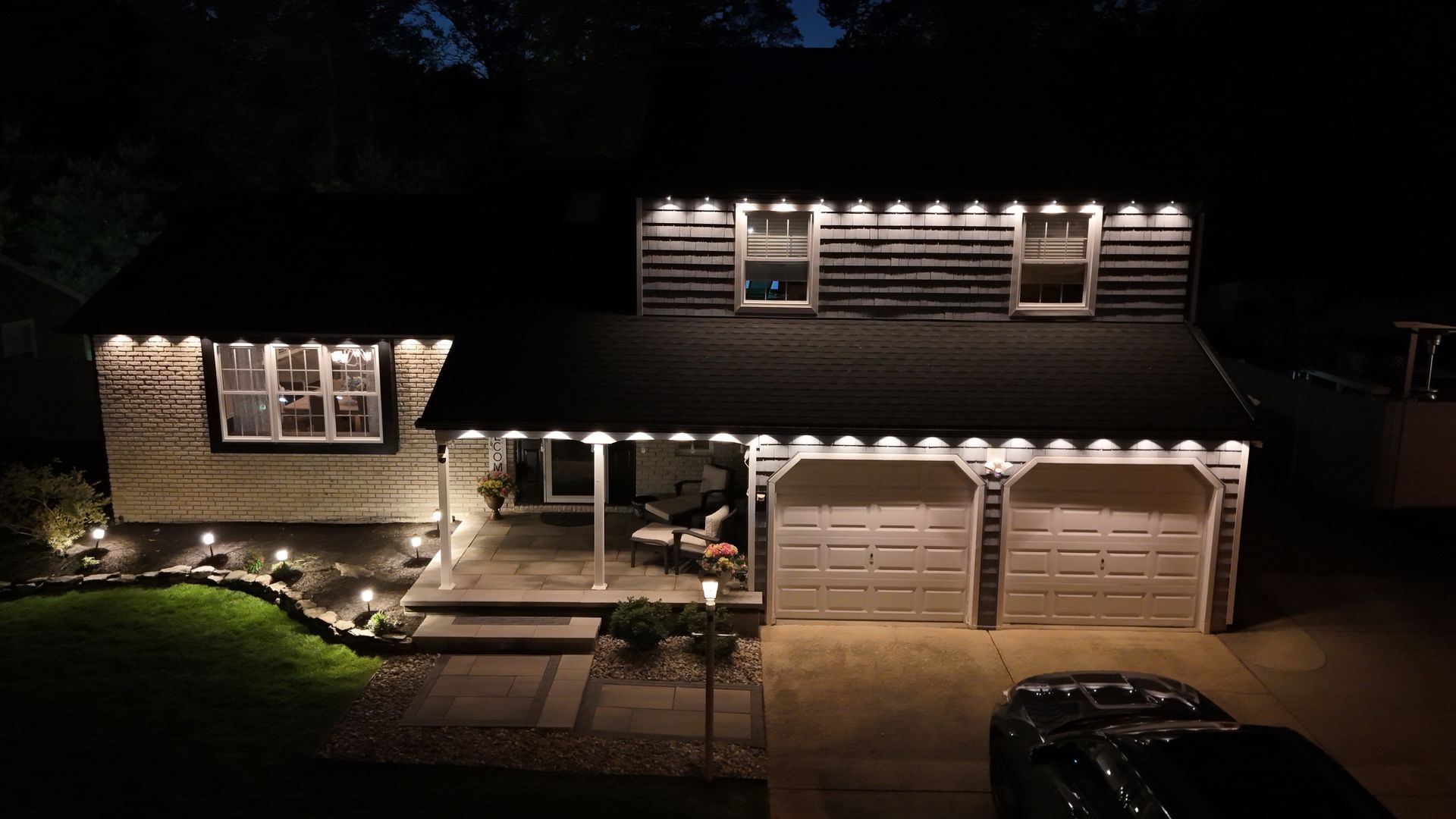 Nighttime view of a two-story house with lit windows, garage, and landscaped front yard.