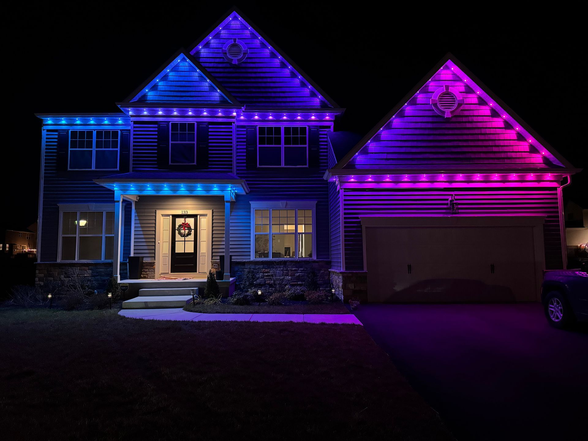 House at night lit with blue and purple decorative lights, with a lit front door and garage