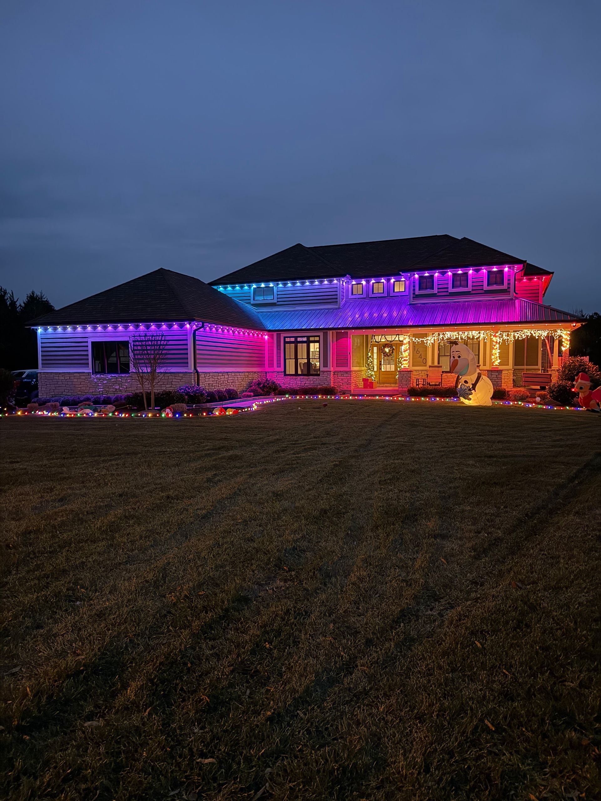 House at dusk lit with purple and warm holiday lights on a grassy hill