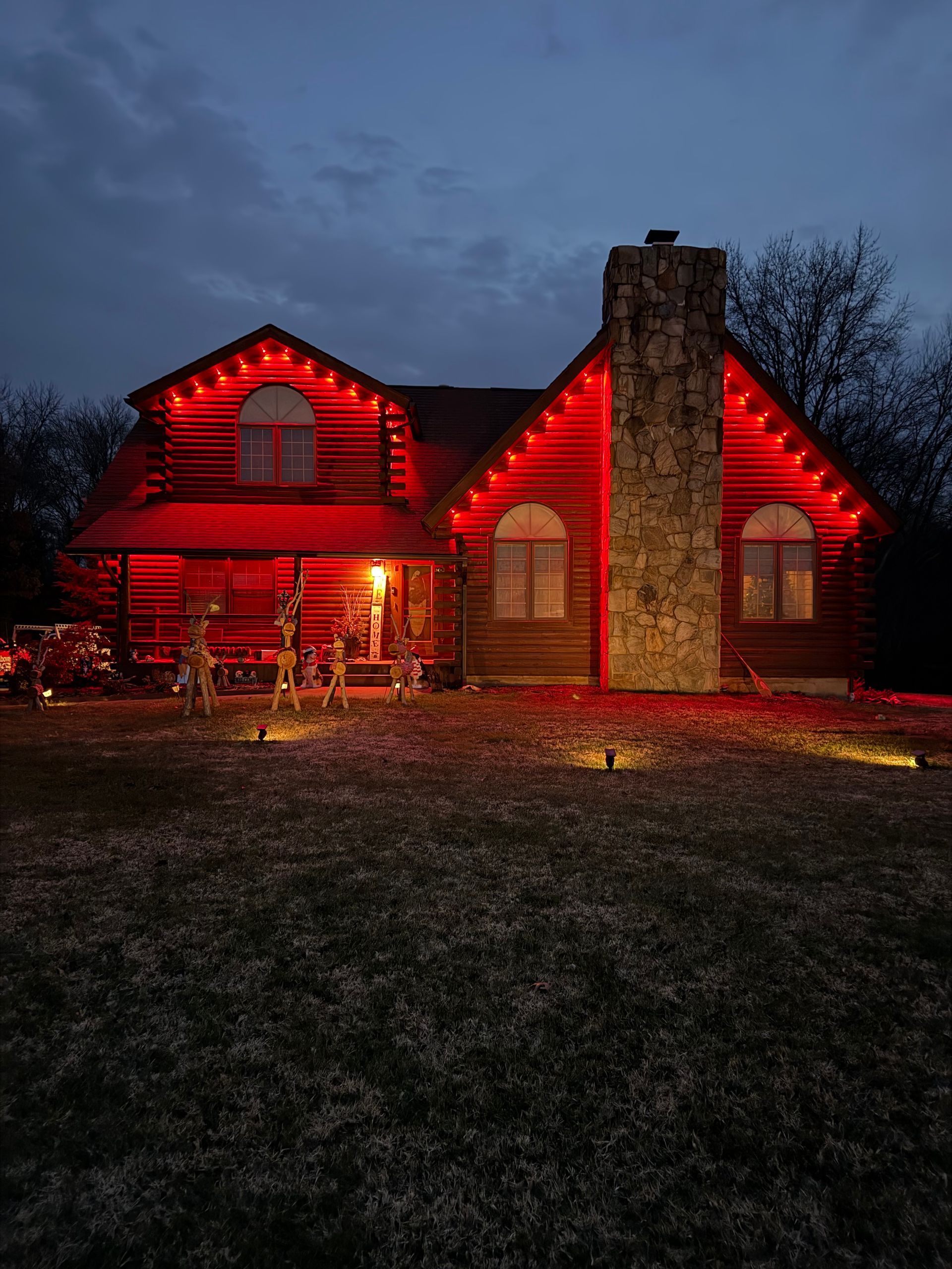 Red house at dusk outlined in red lights, with a stone chimney and dark yard foreground