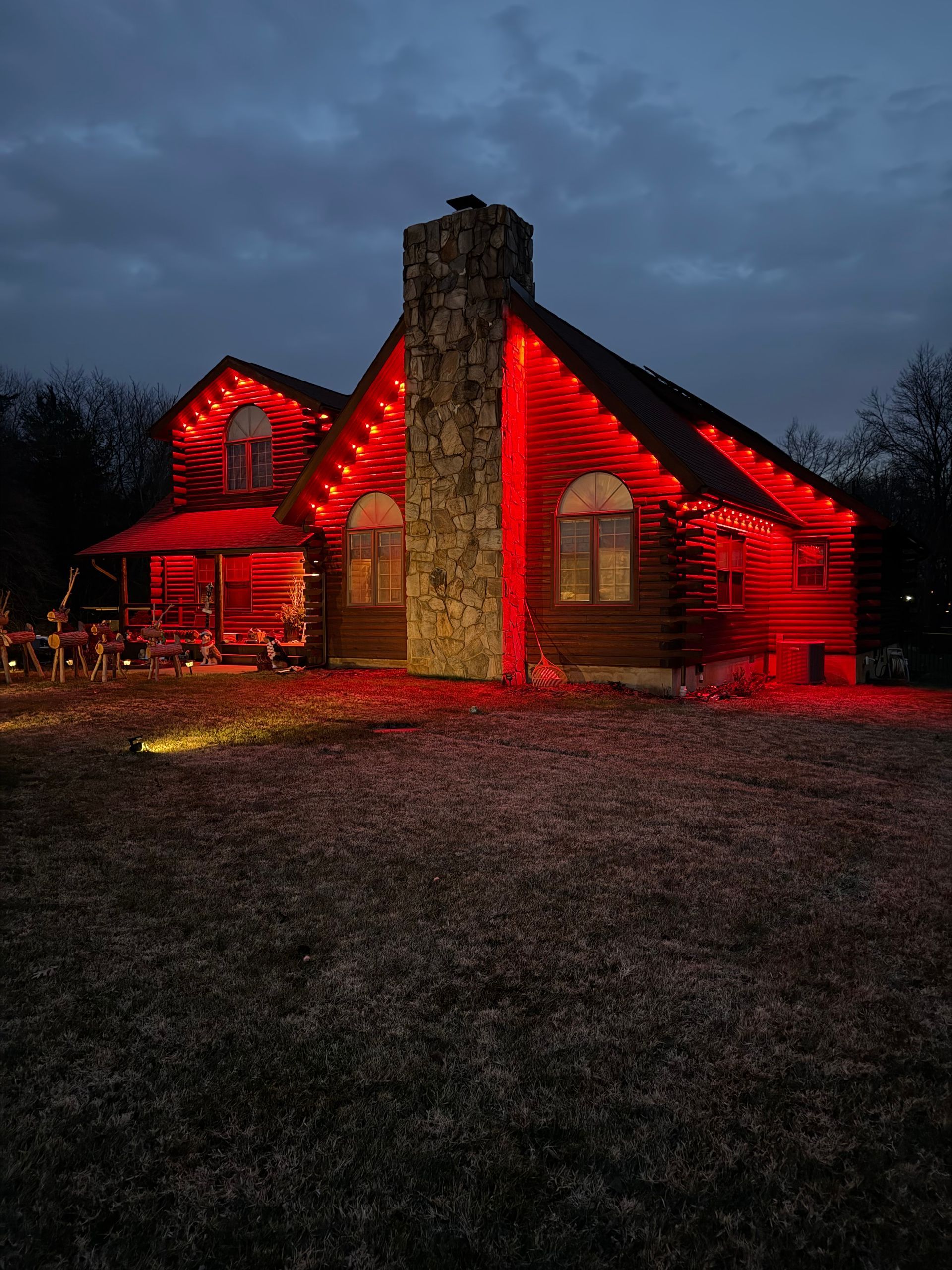 Stone house lit with red lights at dusk, with a tall chimney and cloudy sky