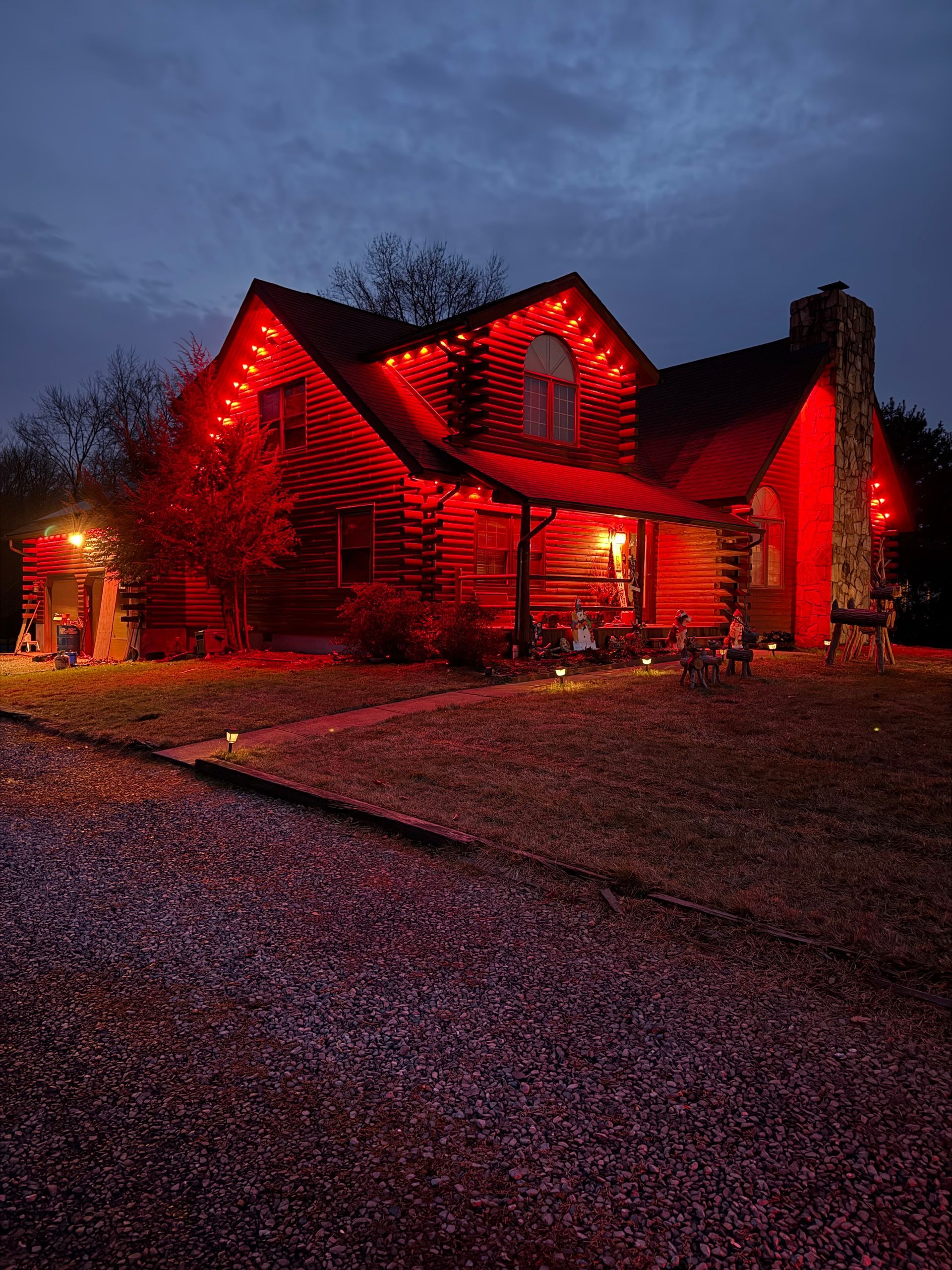 House lit with red lights at dusk, with a gravel driveway and dark sky.