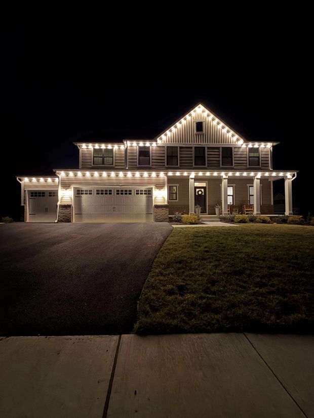 Large house at night with warm Christmas lights, viewed from the street and driveway.