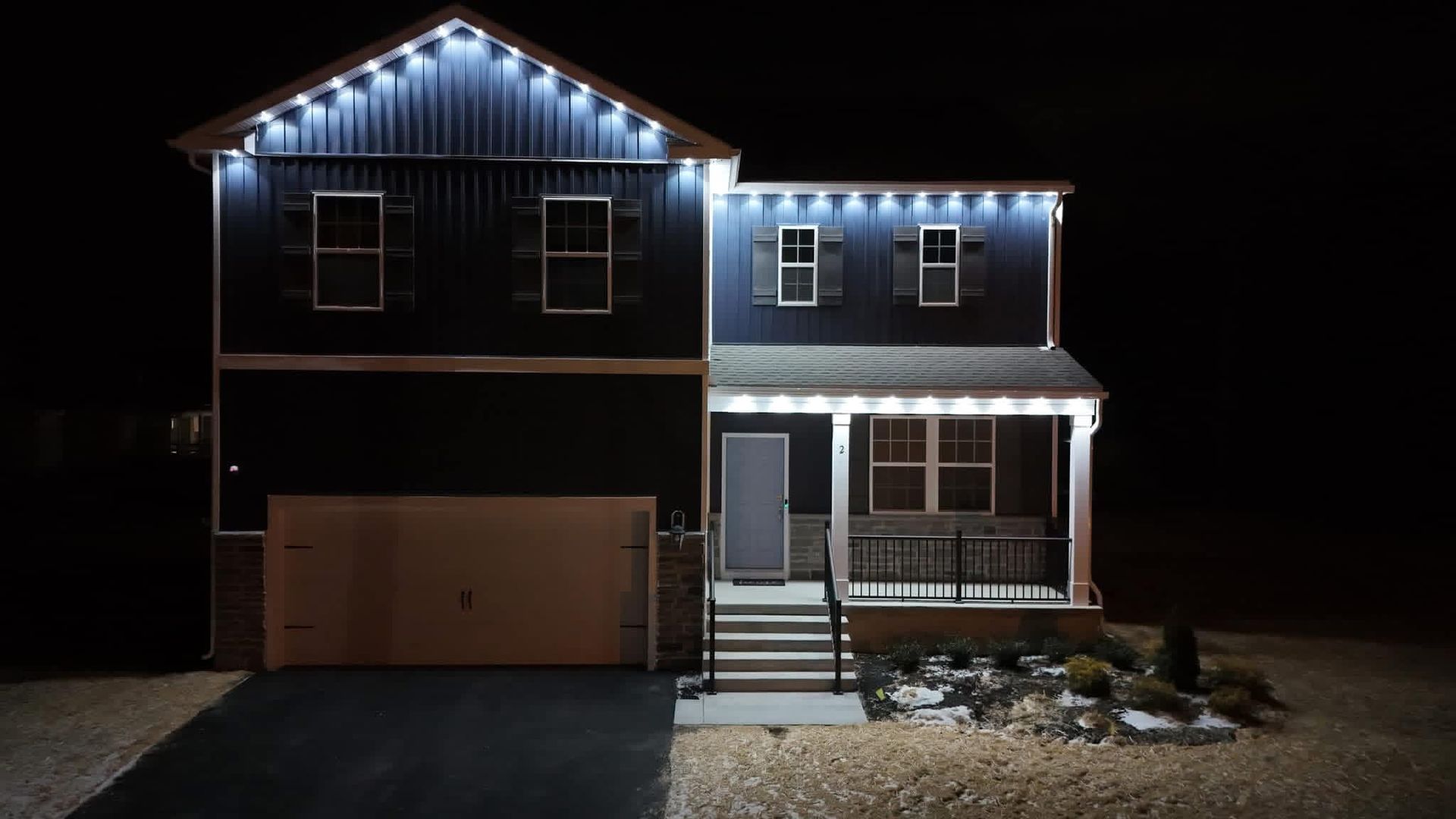 Two-story house at night with white holiday lights along the roof and front porch