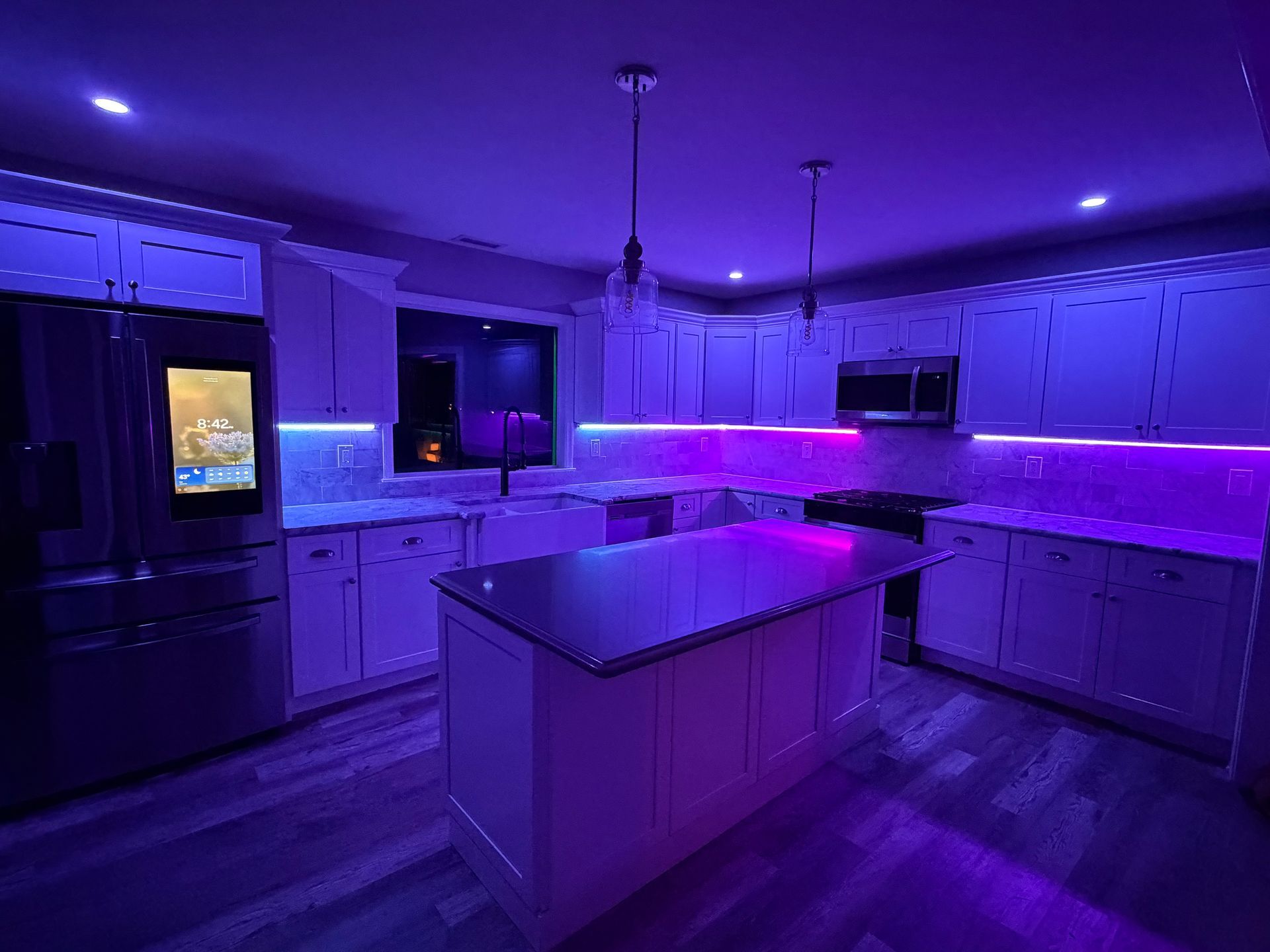 Modern kitchen with purple LED lighting, white cabinets, and a central island at night