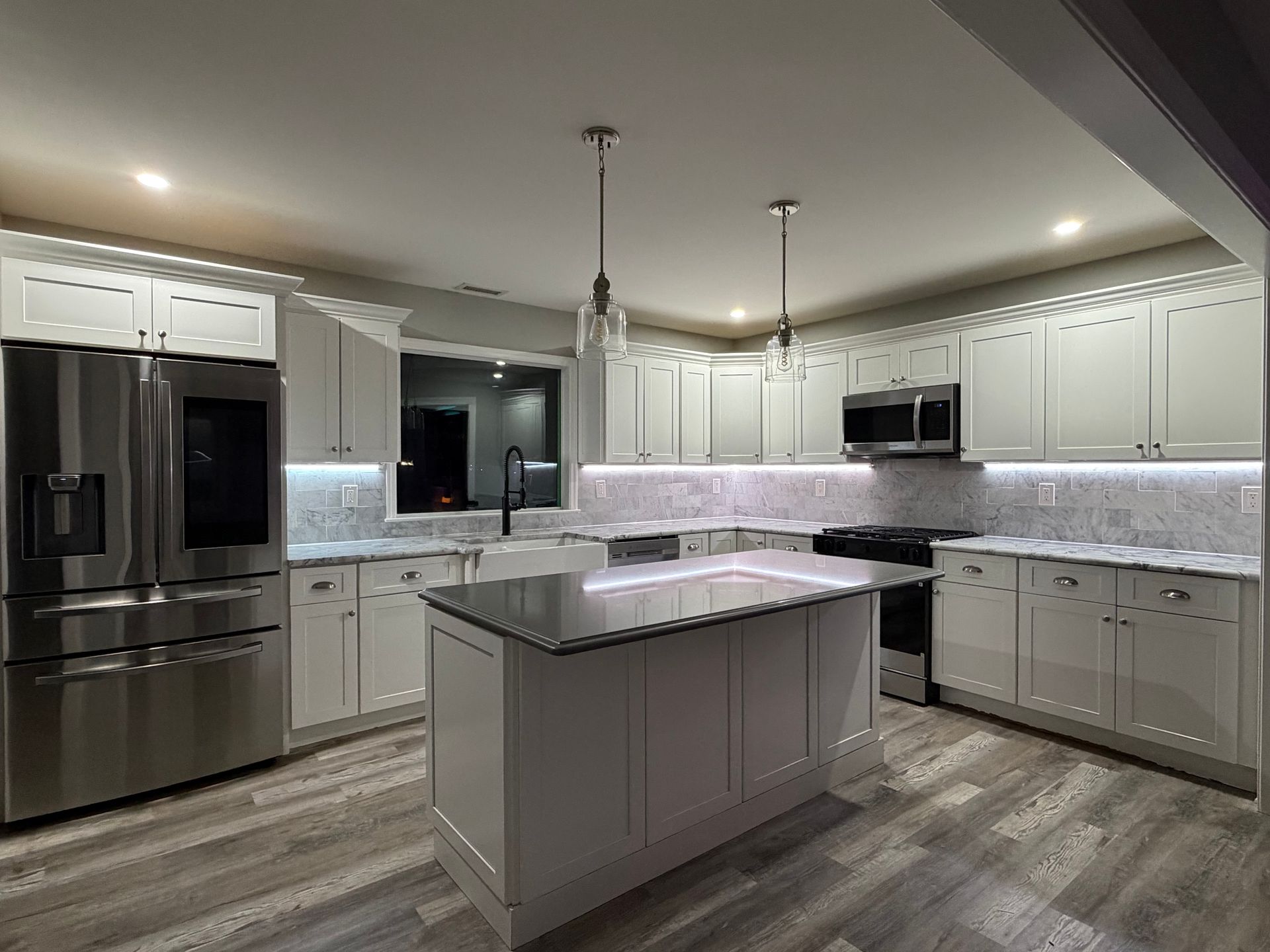Modern gray and white kitchen with island, stainless steel appliances, and under-cabinet lighting