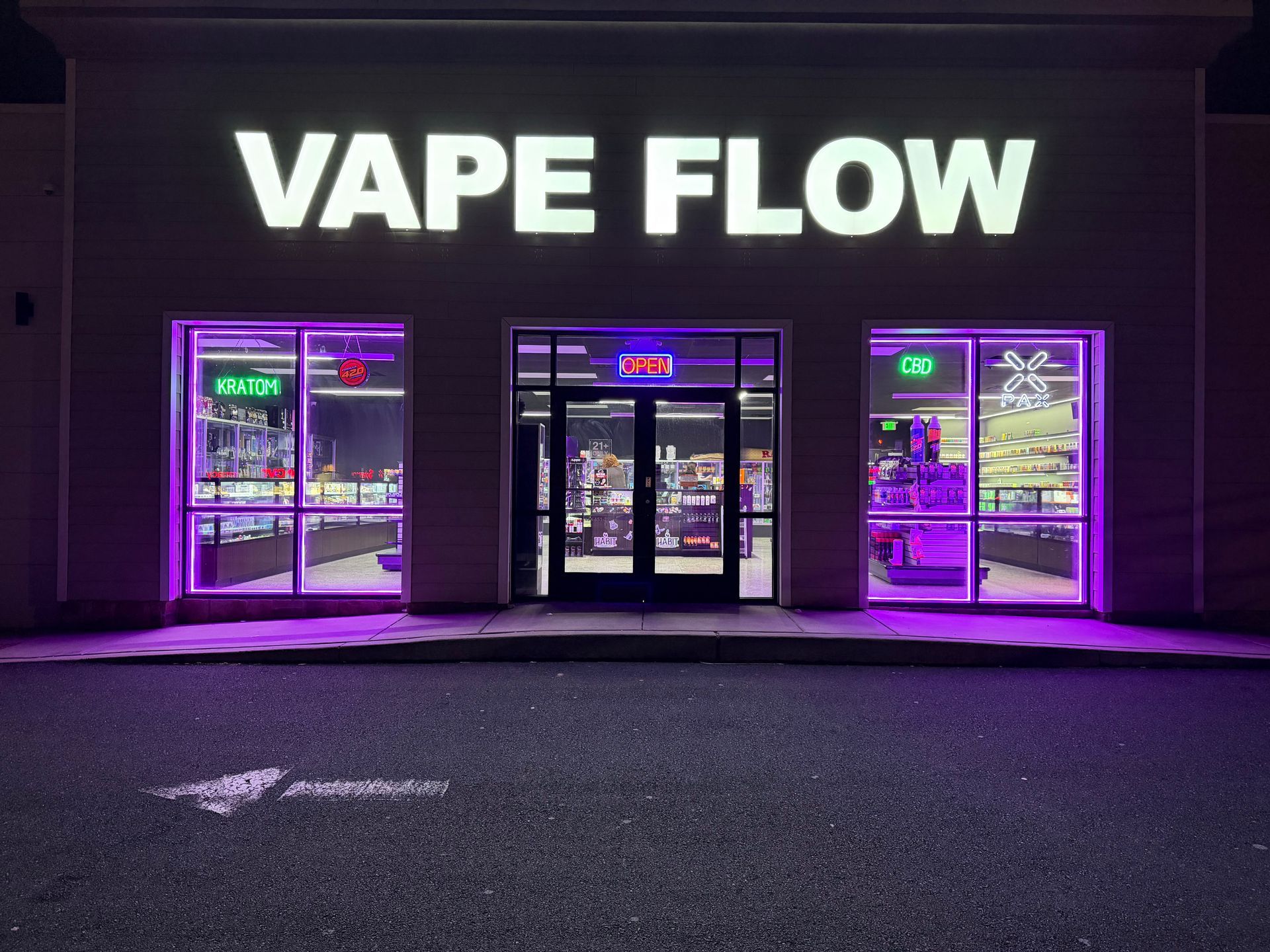 Purple-lit vape shop storefront at night with large “VAPE FLOW” sign and glass doors/windows