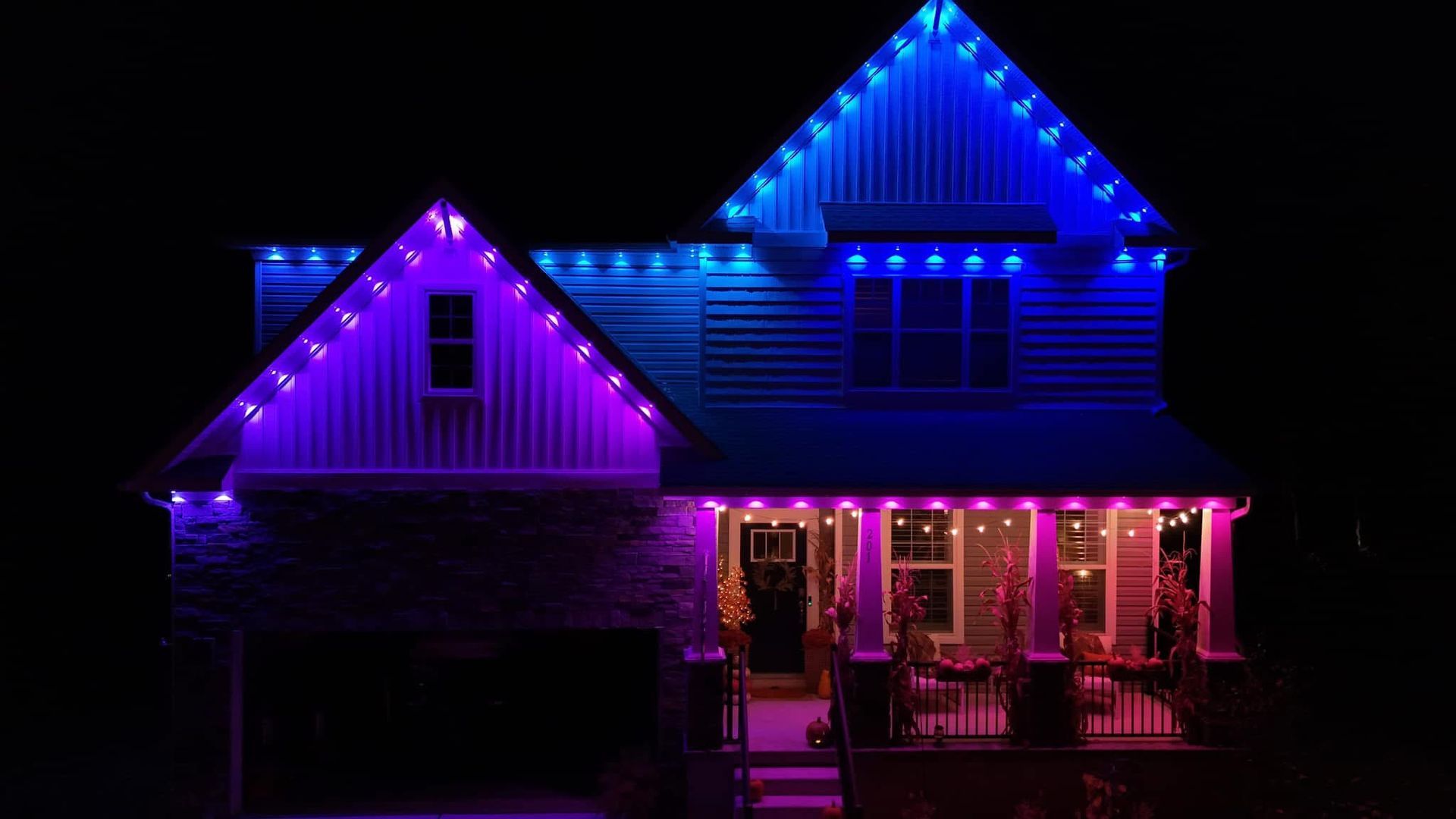 House lit with blue, purple, and pink holiday lights at night
