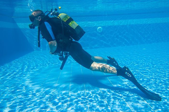 A scuba diver is swimming in a swimming pool.