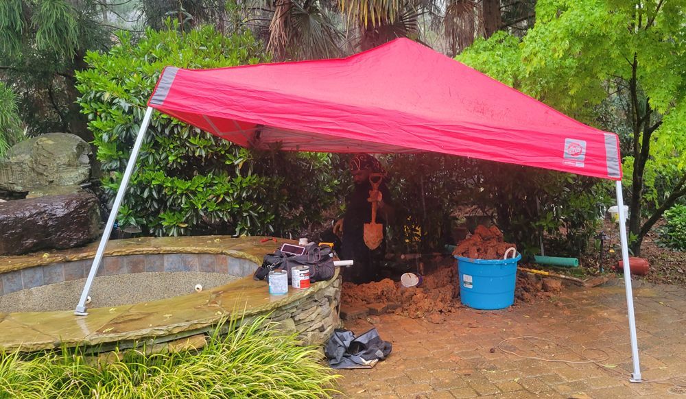 A red tent is sitting next to a pool in the rain.