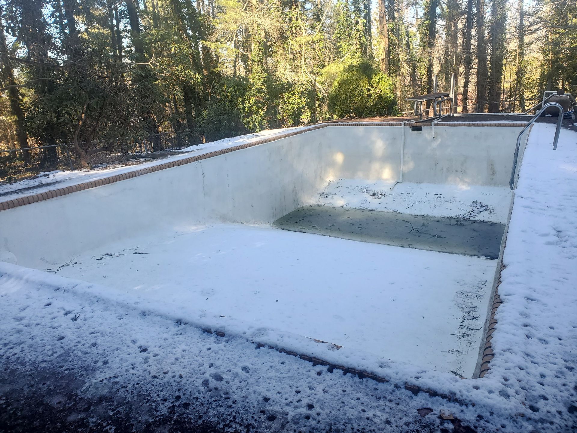 An empty swimming pool covered in snow with trees in the background