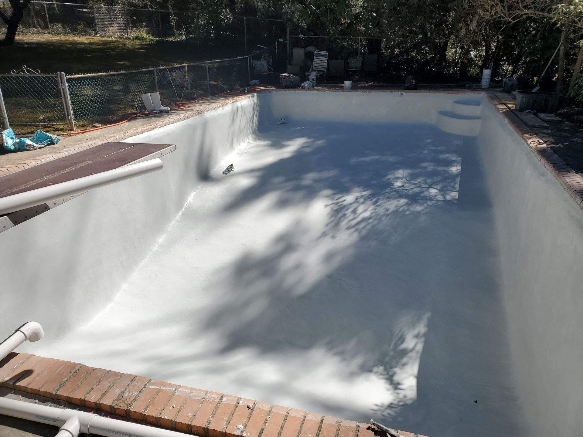 An empty swimming pool with a brick border and a fence in the background