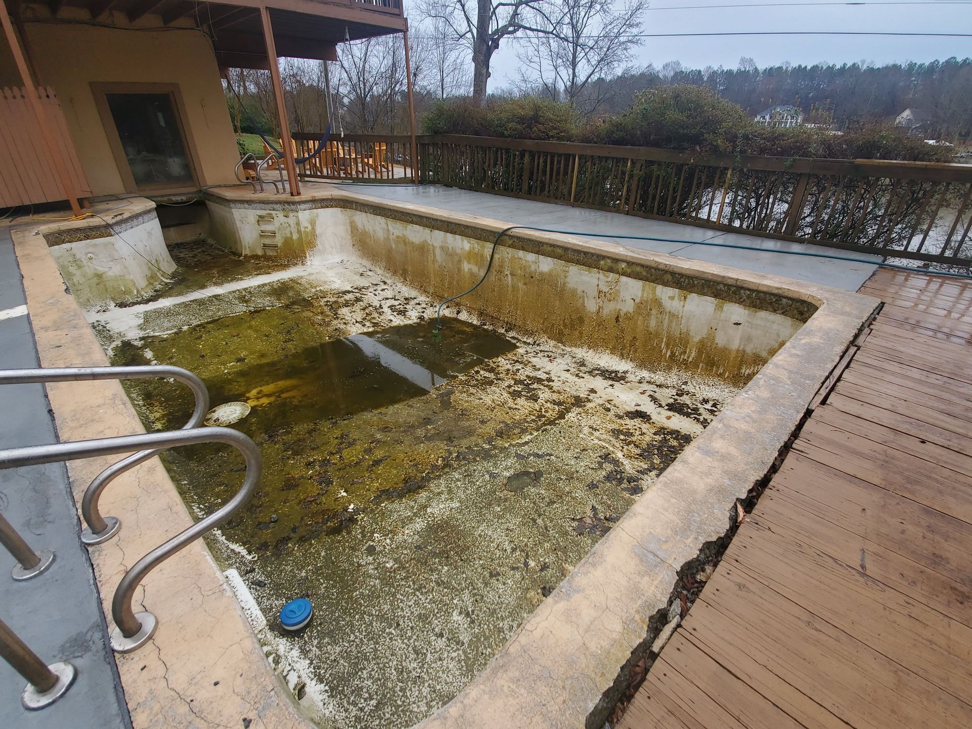 A dirty swimming pool is sitting on a wooden deck next to a house.