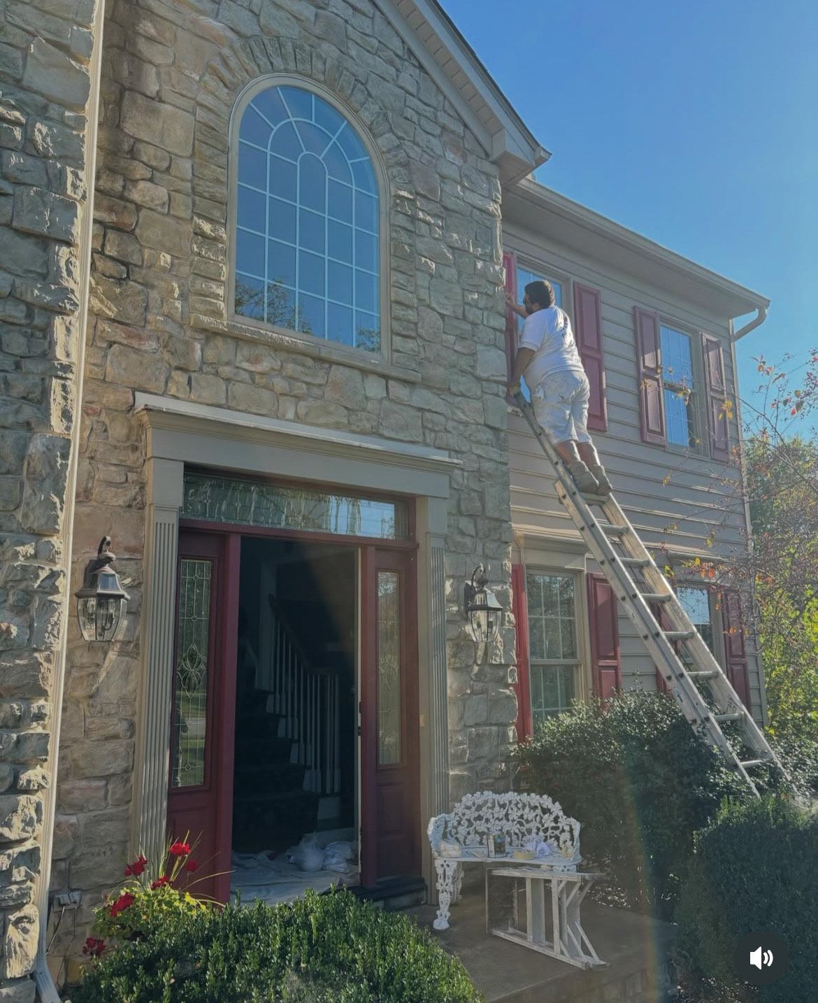 A man on a ladder is painting the side of a house.