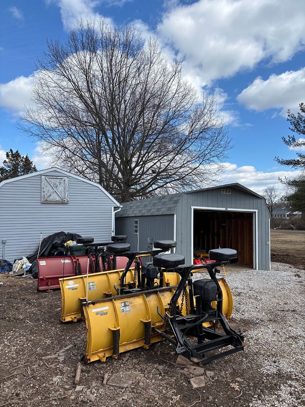 A row of snow plows are parked in front of a garage.