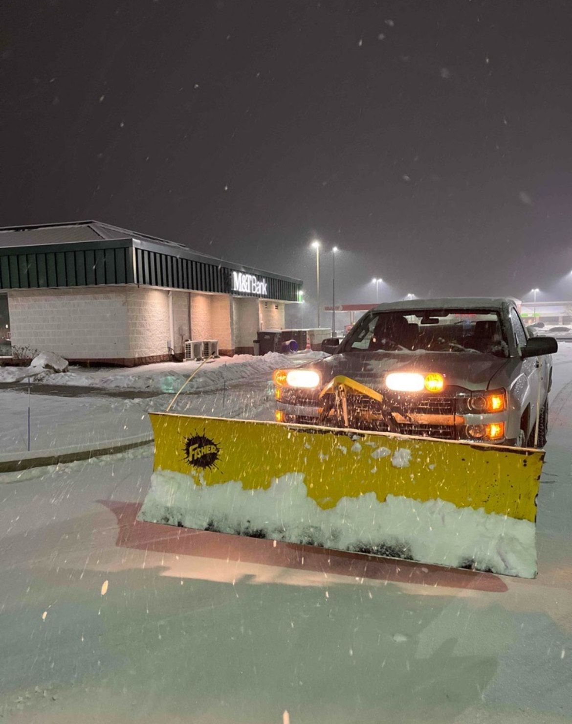A truck is plowing snow in a parking lot at night.