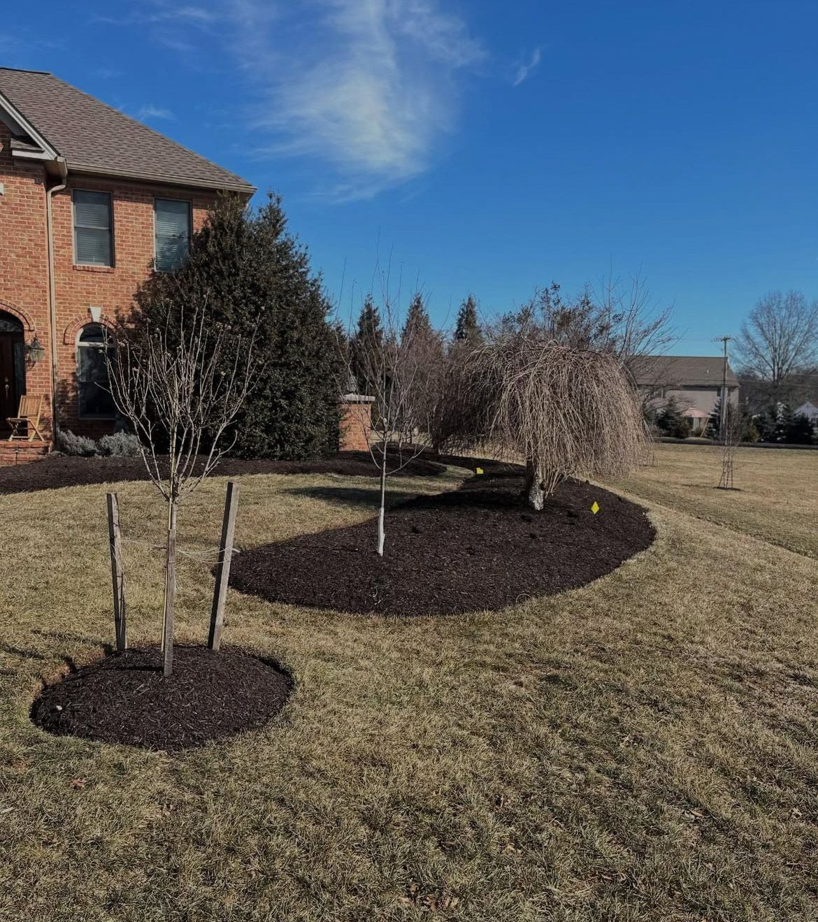 A brick house with a lush green lawn and trees in front of it.