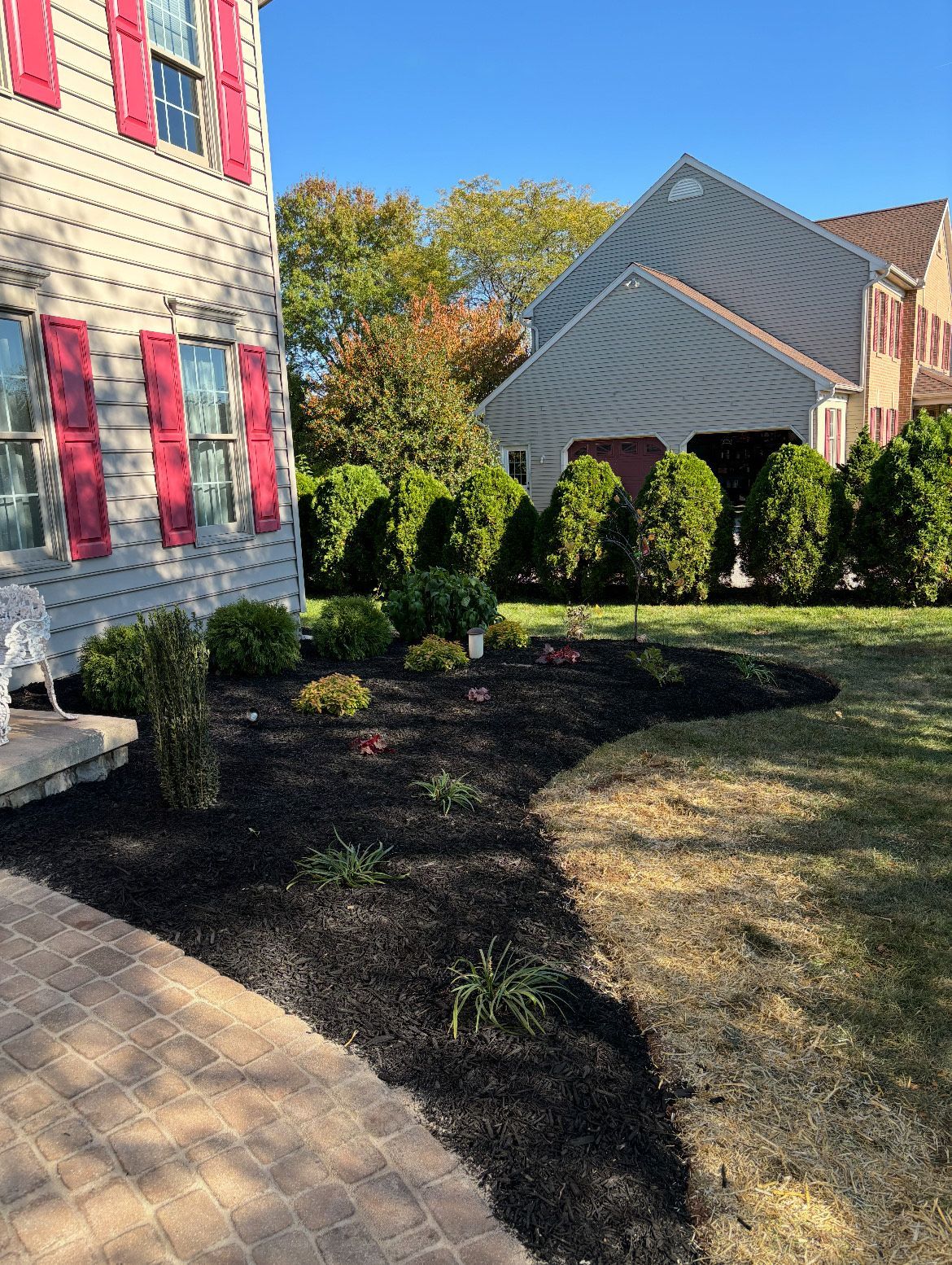 A white house with red shutters and a lush green yard.
