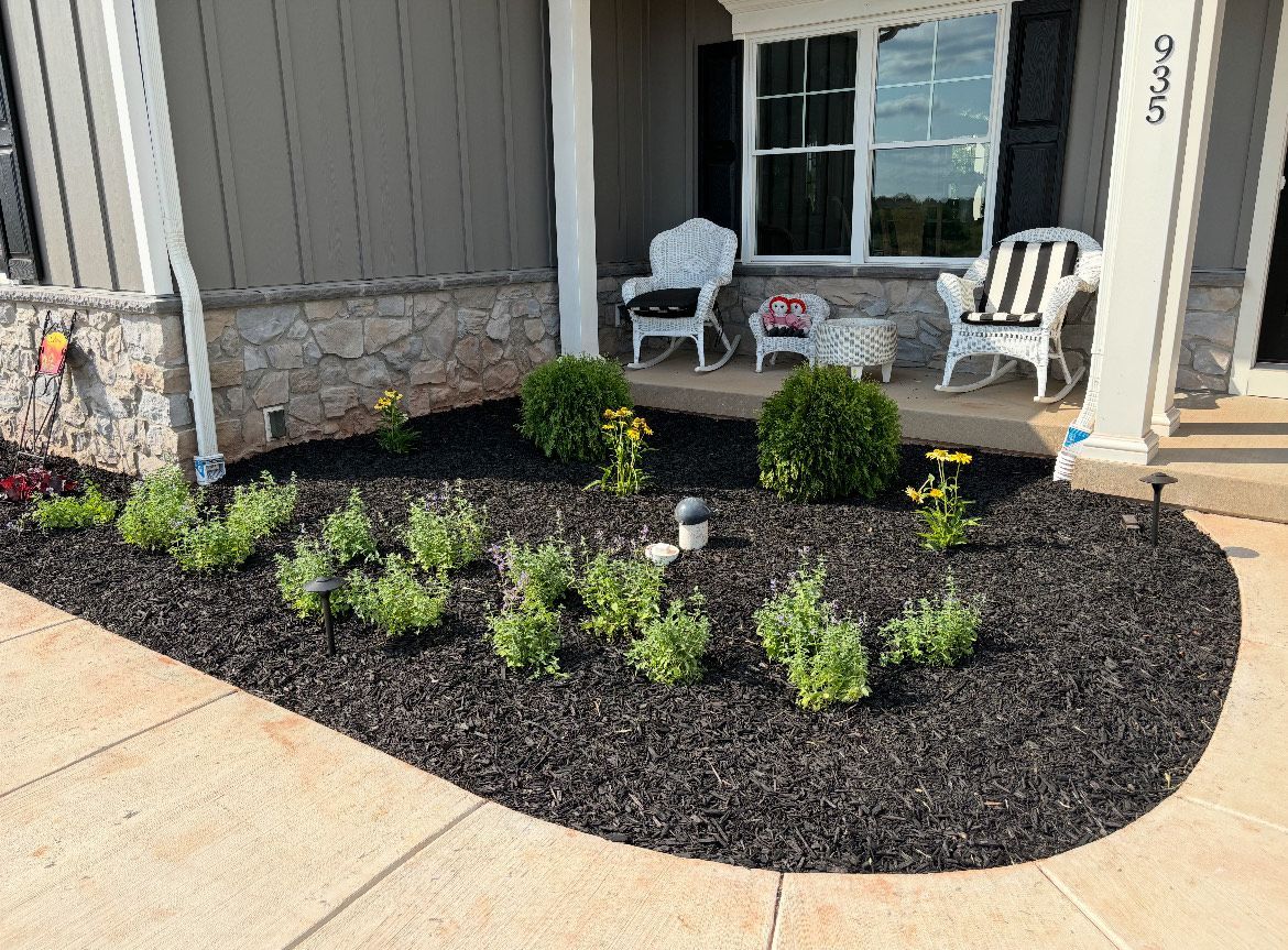 A lawn with a lot of plants and mulch in front of a house.