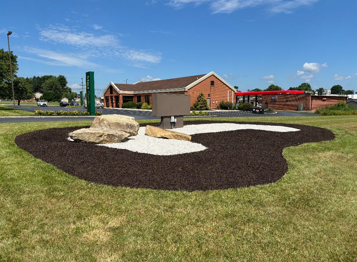 A large rock in the middle of a grassy field in front of a building.
