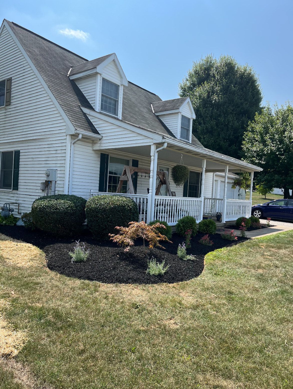 A white house with a porch and a car parked in front of it.