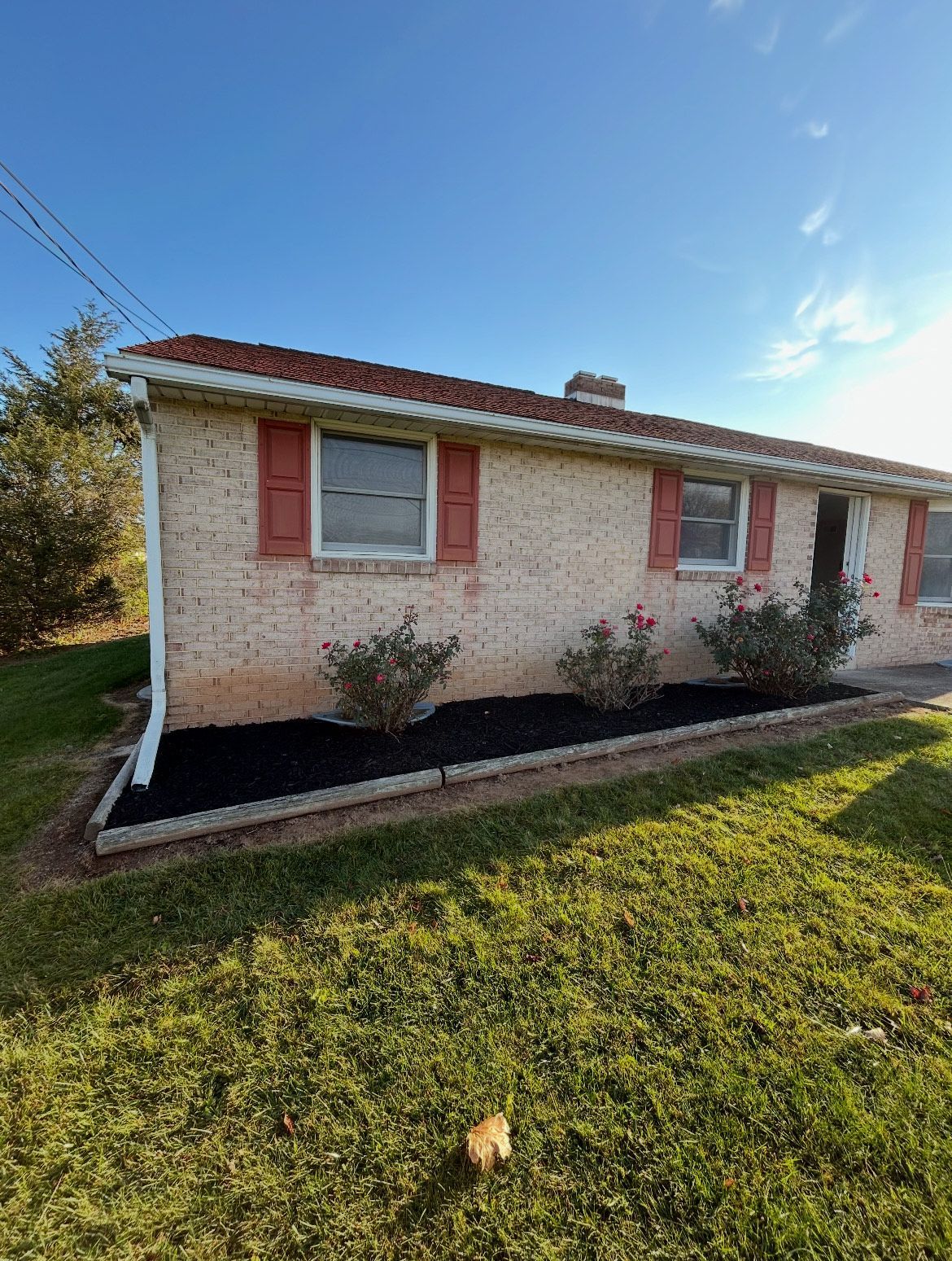A brick house with red shutters is sitting on top of a lush green lawn.