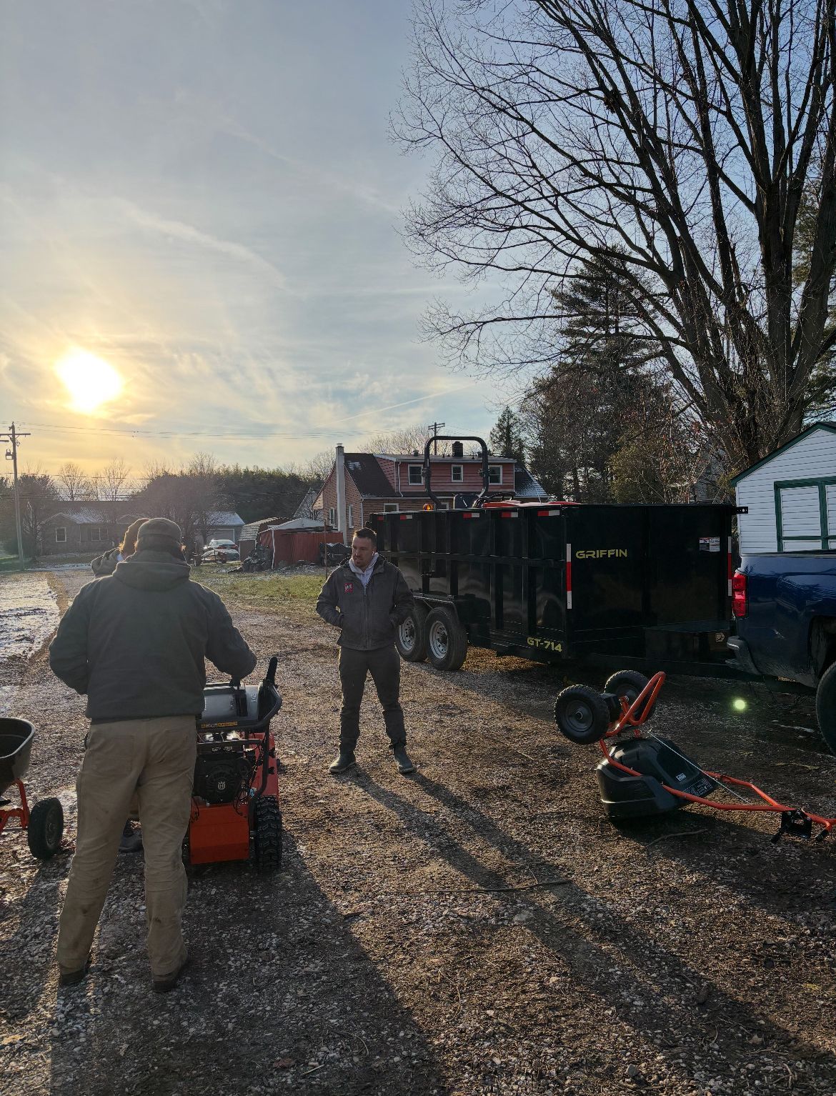 A man is standing next to a lawn mower in a parking lot.