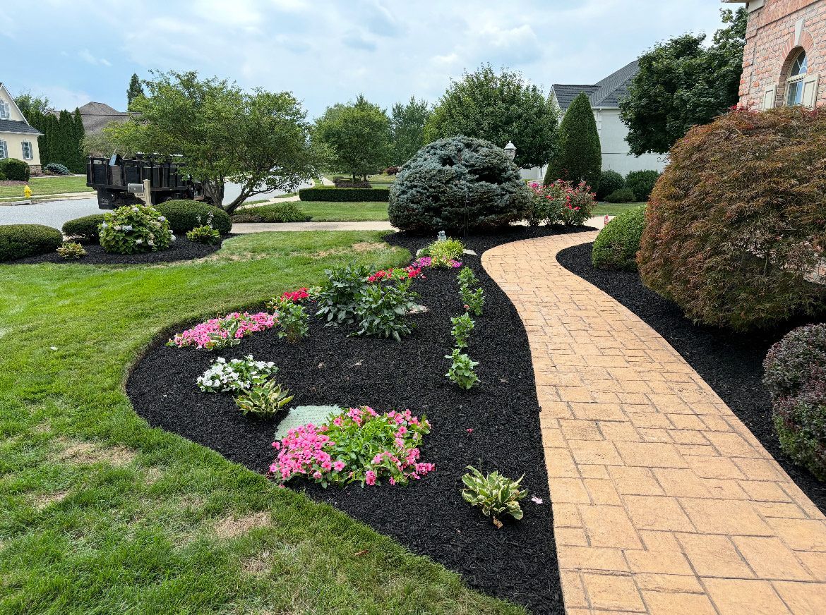 A brick walkway leading to a house surrounded by flowers and bushes.